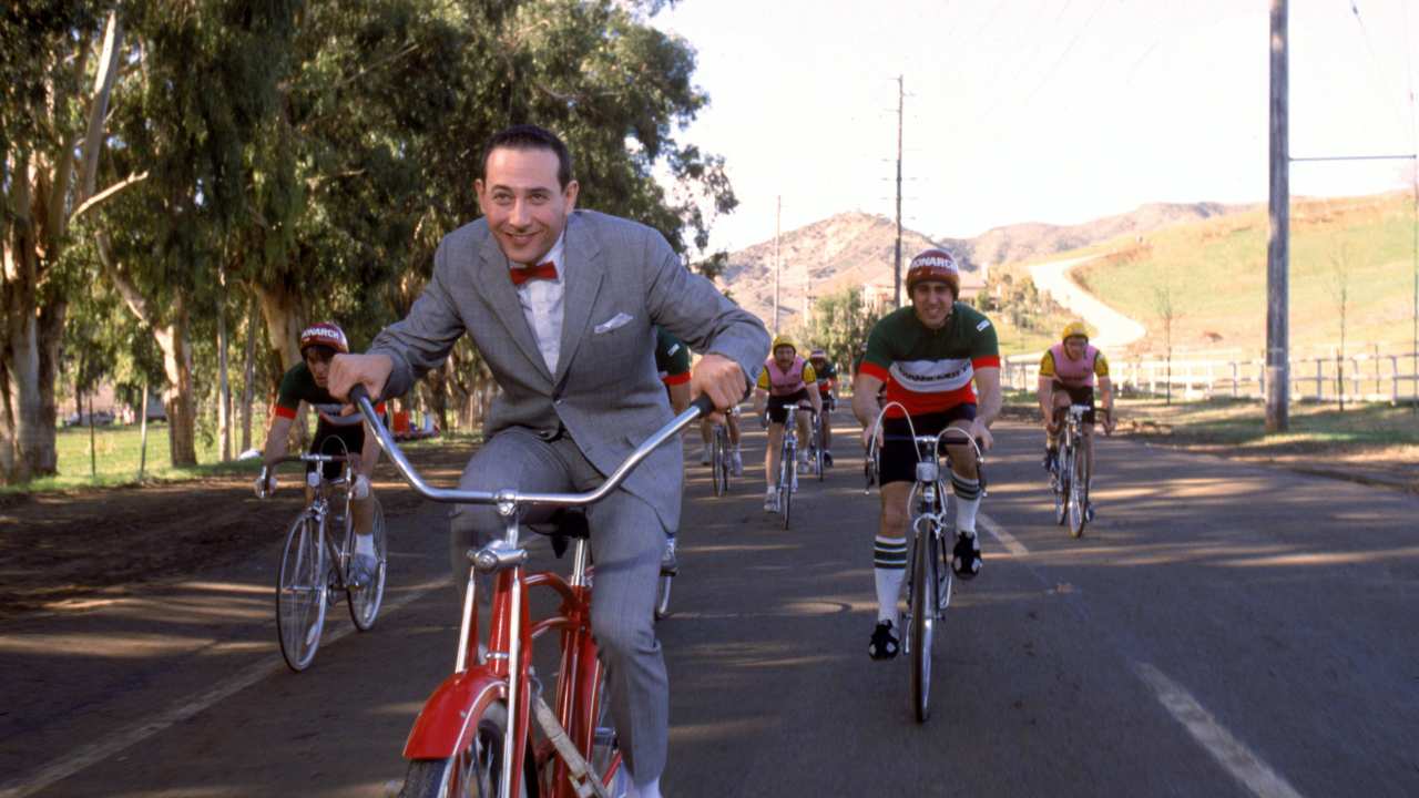 a man wearing a grey suit and bowtie on a bike